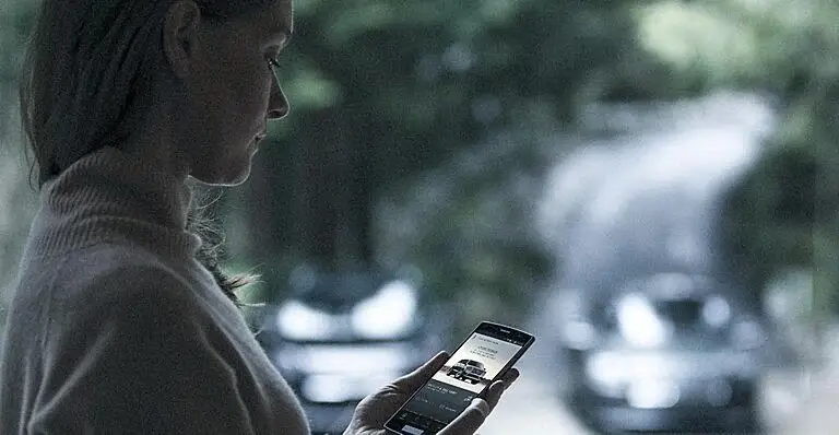 Woman checking vehicle information on smartphone with cars in background