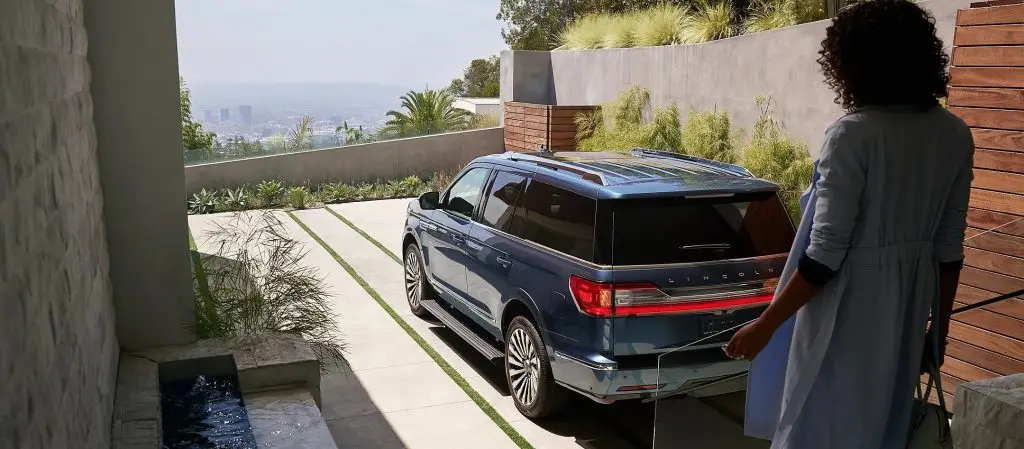 Blue Lincoln Navigator SUV parked in driveway of modern hillside home