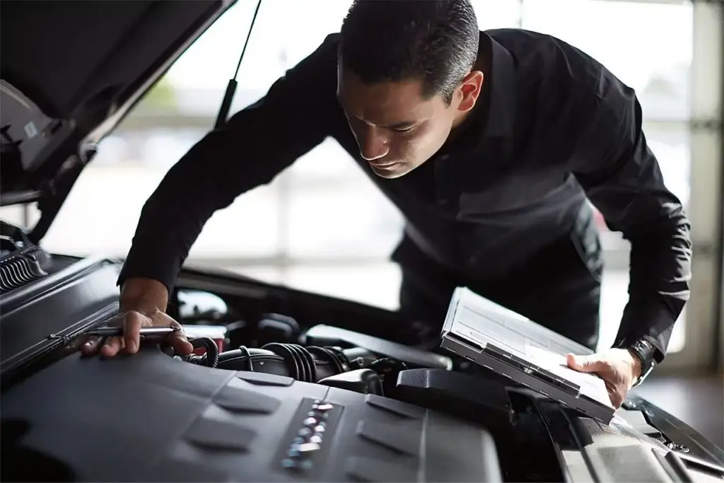 Lincoln service technician inspecting engine bay while using diagnostic tablet