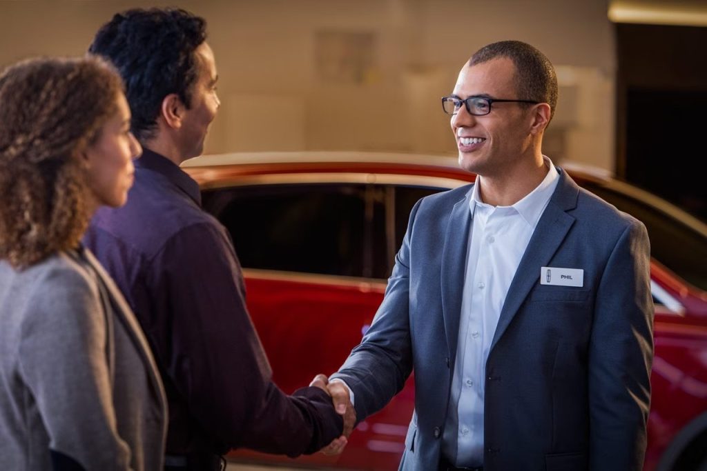 Lincoln sales advisor Phil shaking hands with customers beside red vehicle