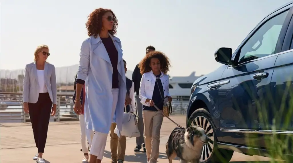 Family walking dog beside blue Lincoln Navigator SUV at marina