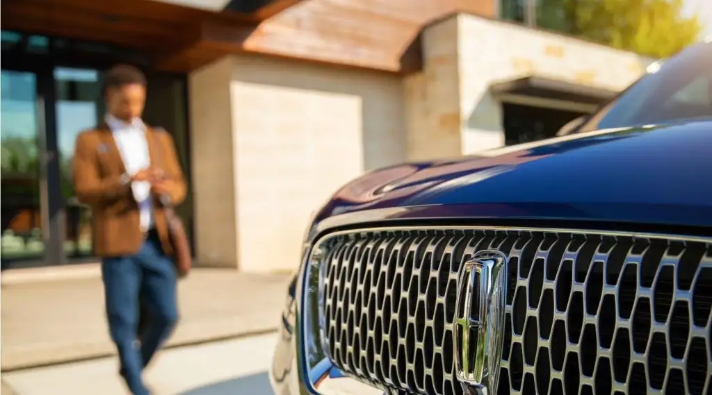 Close-up of Lincoln grille and emblem with man approaching modern home