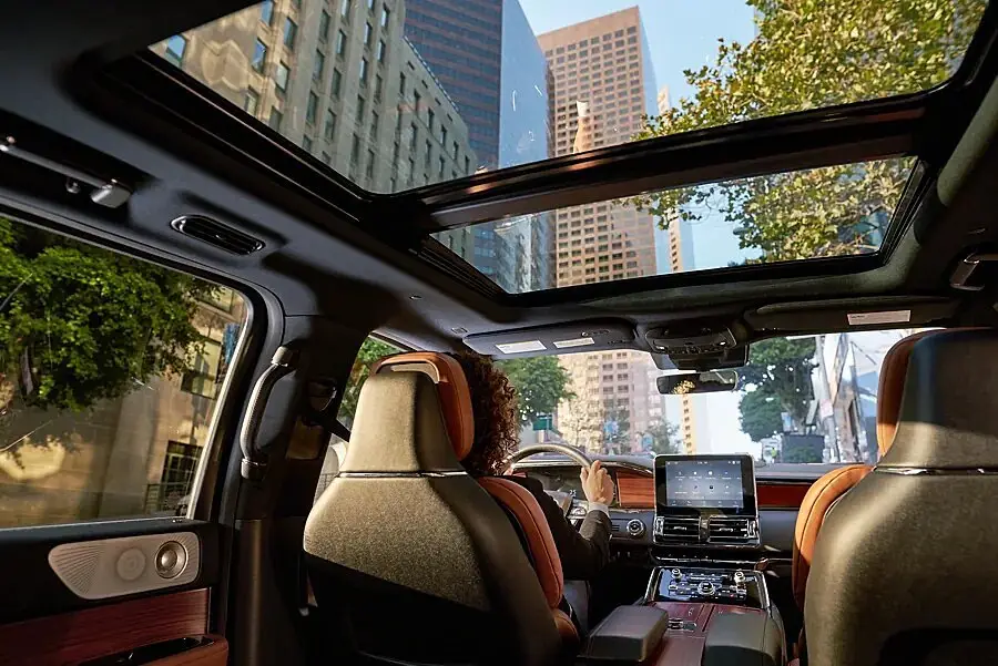 Lincoln SUV cabin showing tan leather seats and glass roof over city street