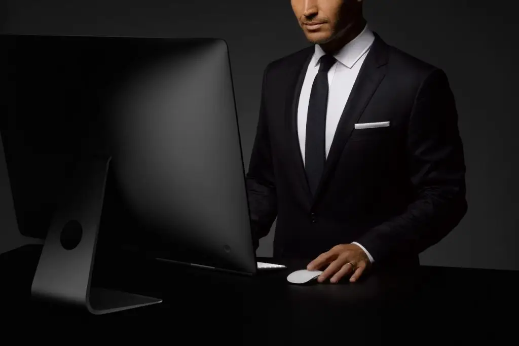 Businessman in suit working at desk with computer in dark studio setting