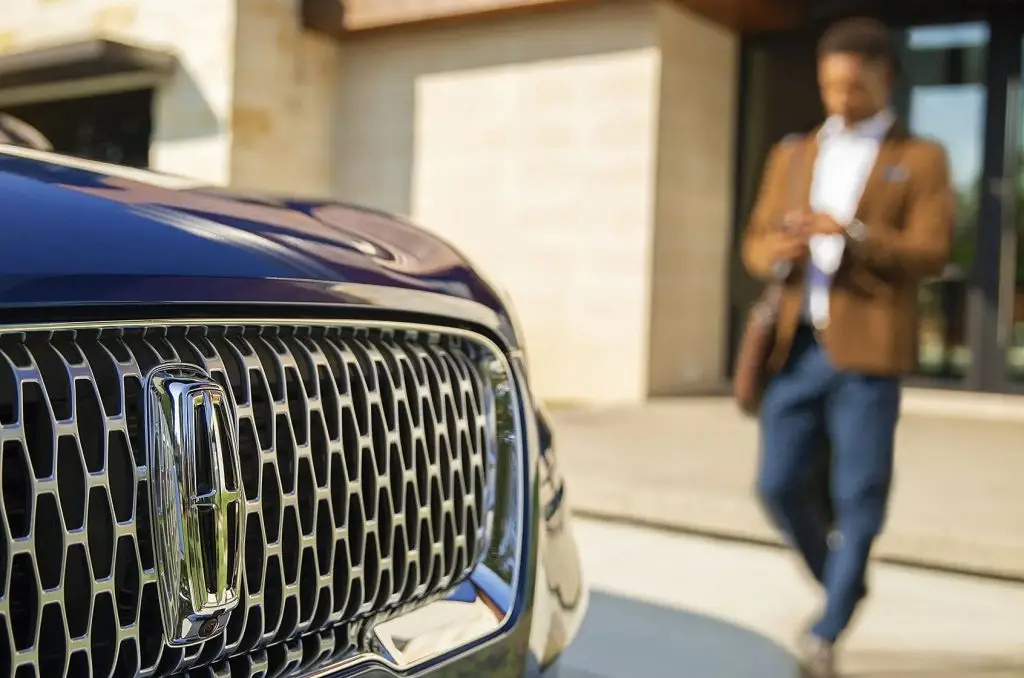 Close-up of Lincoln grille badge with valet checking phone outside luxury building