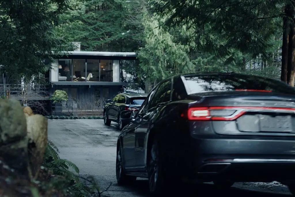 Two dark Lincoln sedans parked outside modern forest home at dusk