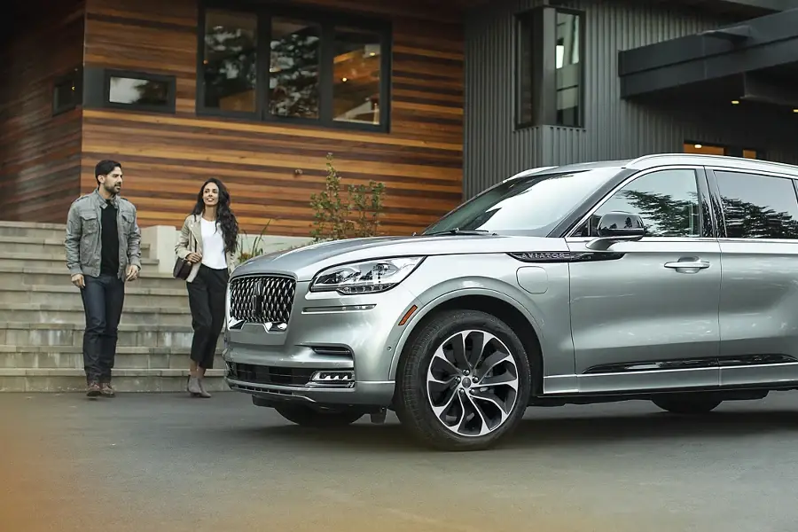 Couple walking toward silver Lincoln Aviator parked outside modern home