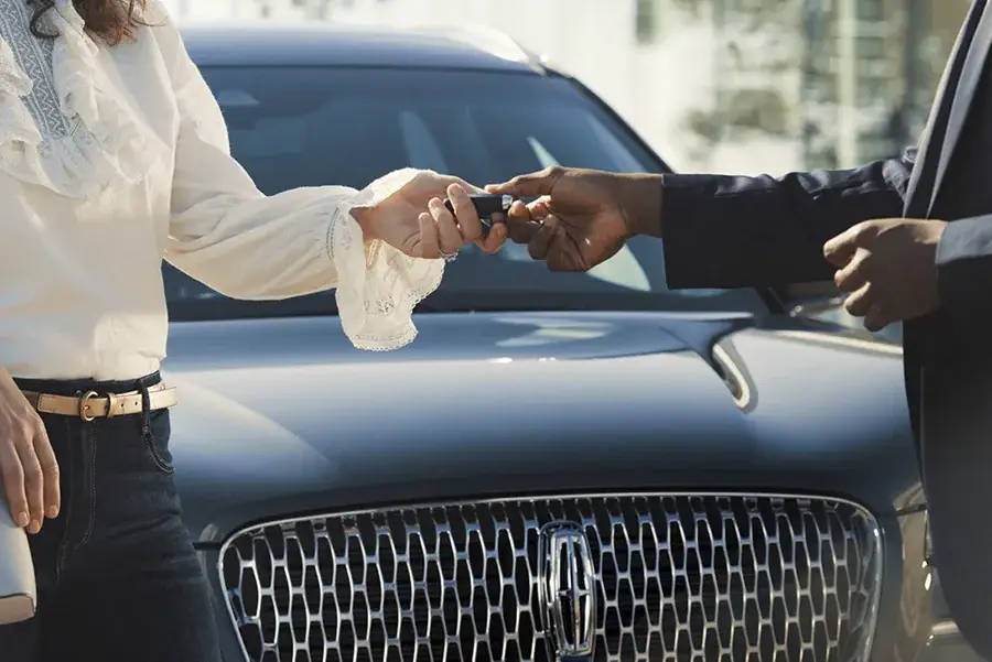Salesperson handing over car keys to customer in front of Lincoln SUV grille